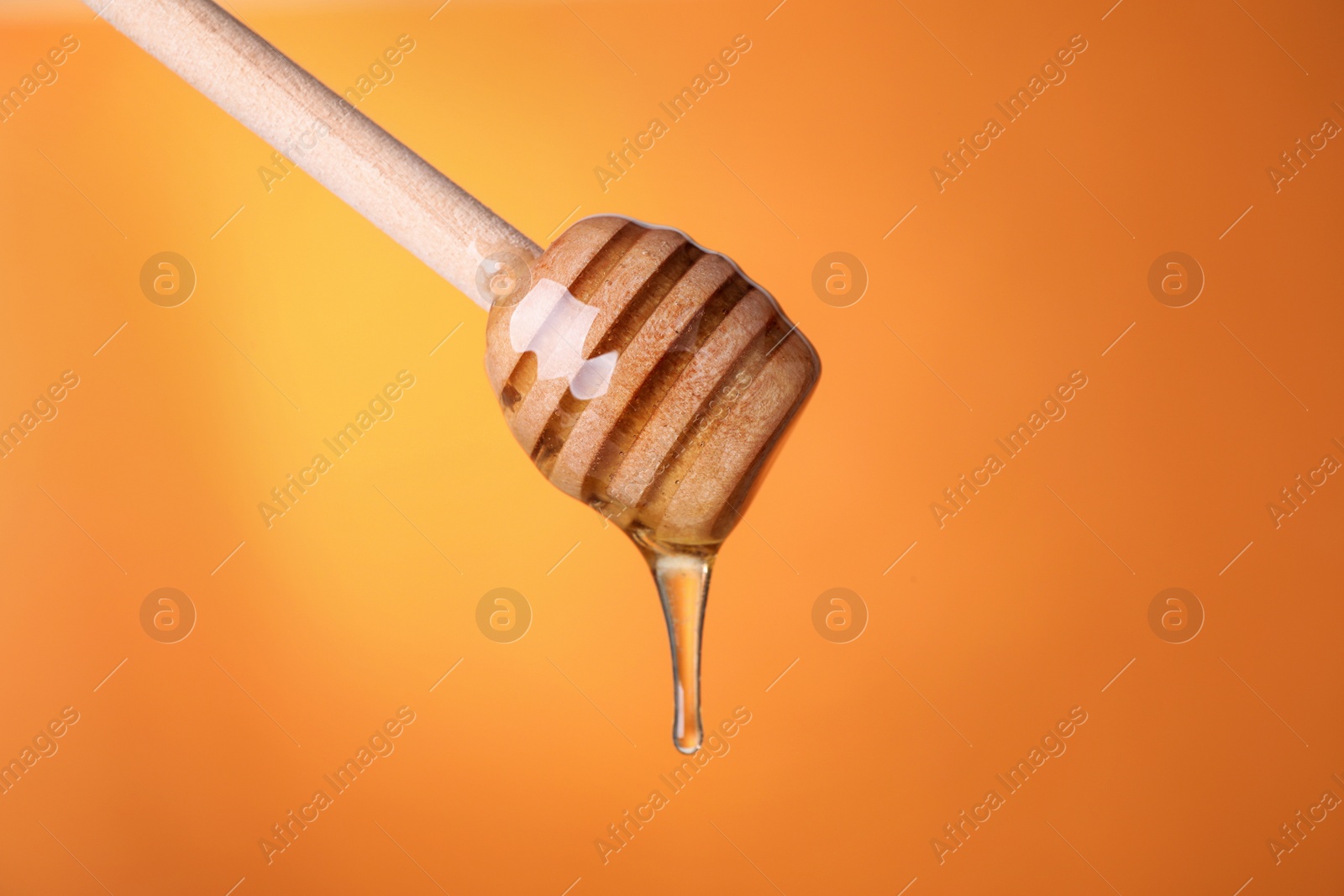 Photo of Dripping honey from wooden dipper on orange background, closeup