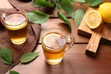 Cups of tasty iced tea with lemon, fresh fruits and green leaves on wooden table