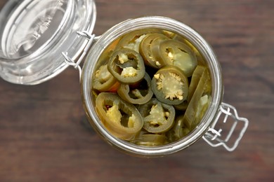 Photo of Glass jar of pickled green jalapeno peppers on wooden table, top view