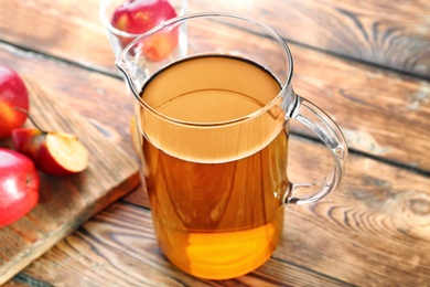 Jug with fresh apple juice on wooden table