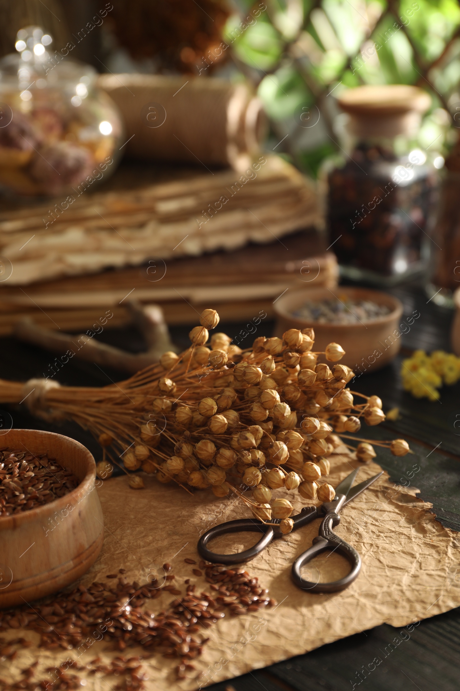 Photo of Flax seeds with dry flowers and scissors on black table indoors