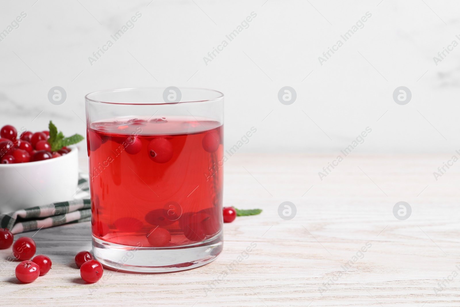 Photo of Tasty cranberry juice in glass and fresh berries on white wooden table. Space for text