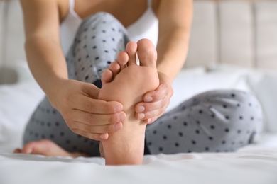 Photo of Young woman suffering from pain in foot on bed, closeup
