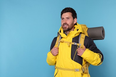 Happy tourist with backpack on light blue background, space for text
