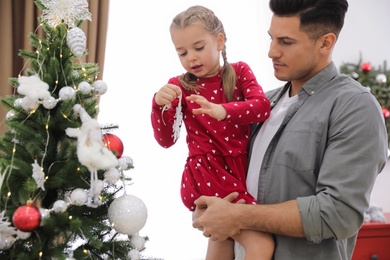 Father with his cute daughter decorating Christmas tree together at home