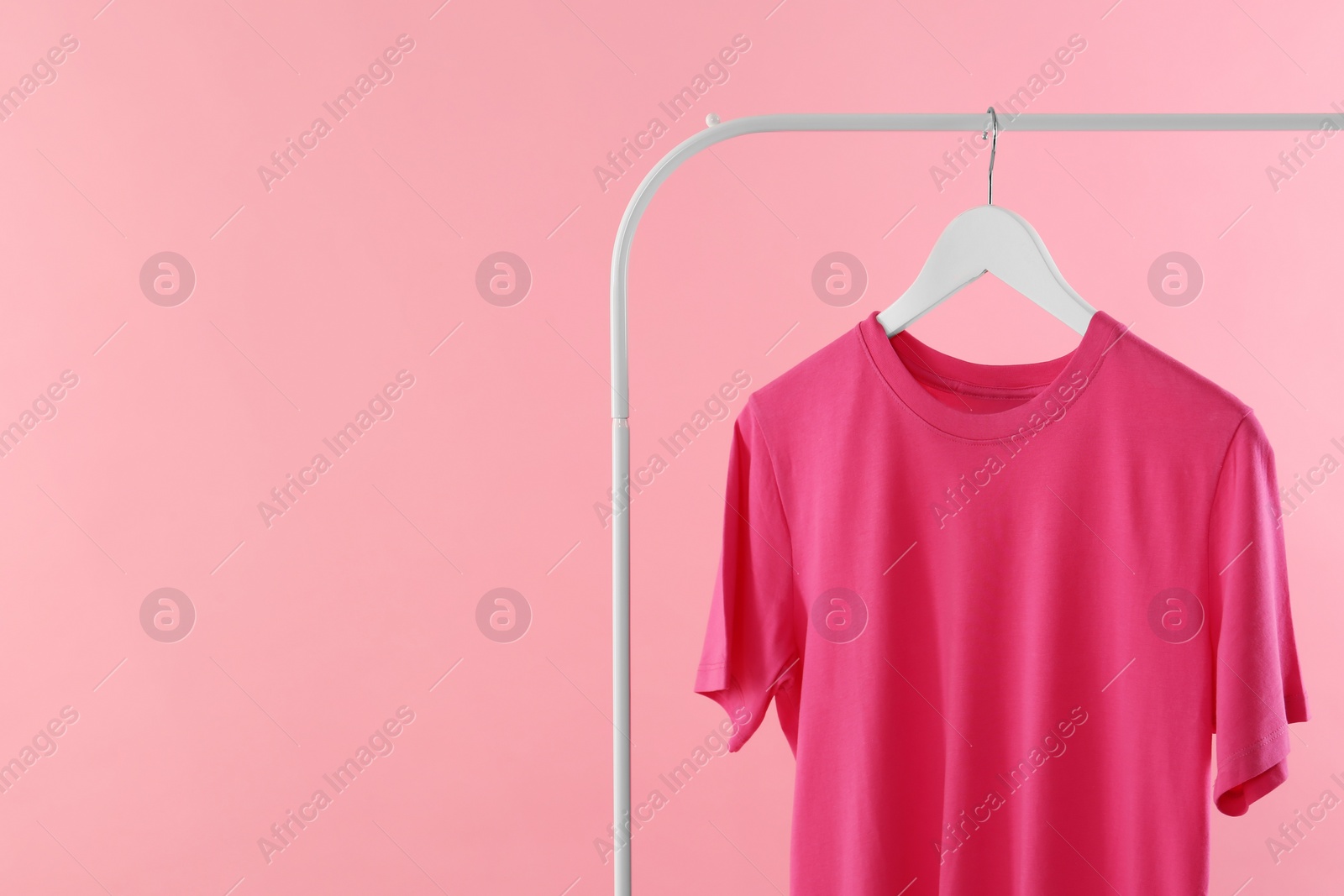 Photo of Rack with stylish t-shirt on pink background. Space for text