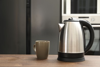 Photo of Modern electric kettle and cup on table in kitchen. Space for text