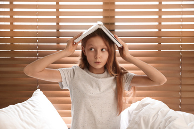 Photo of Emotional preteen girl with book on bed near window