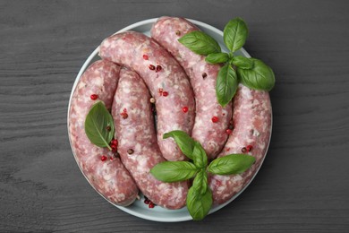 Raw homemade sausages, basil leaves and peppercorns on grey wooden table, top view