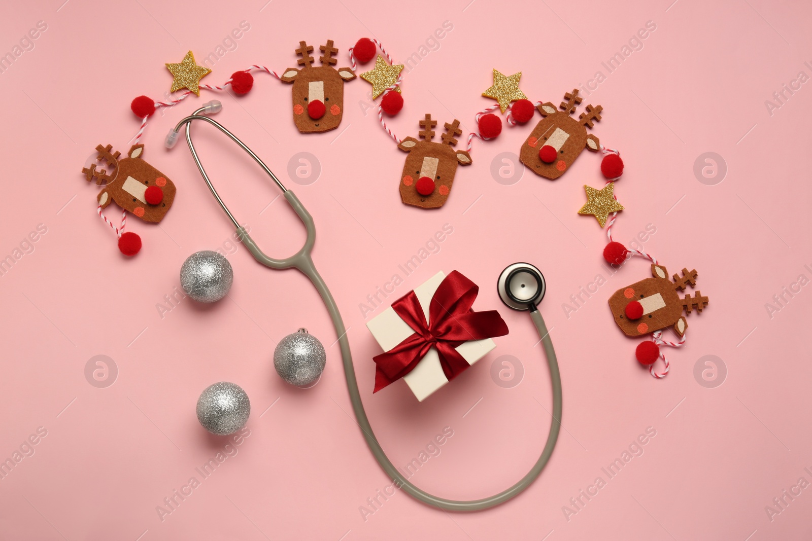 Photo of Greeting card for doctor with stethoscope, gift box and Christmas decor on pink background, flat lay