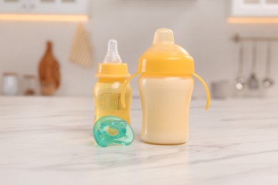 Photo of Baby bottles and pacifier on white marble table indoors. Maternity leave concept