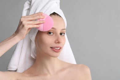 Washing face. Young woman with cleansing brush on grey background, space for text