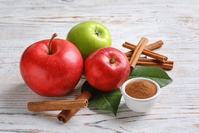 Fresh apples with cinnamon sticks and powder on wooden table