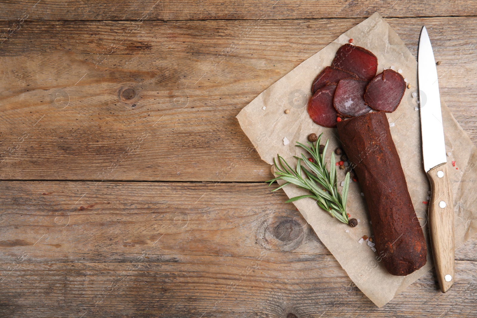 Photo of Delicious dry-cured beef basturma and knife on wooden table, top view. Space for text