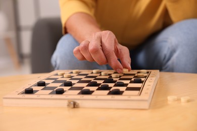 Photo of Woman playing checkers at wooden table indoors, closeup