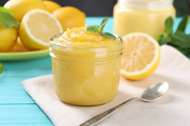 Photo of Delicious lemon curd in glass jar, fresh citrus fruits, mint and spoon on light blue wooden table