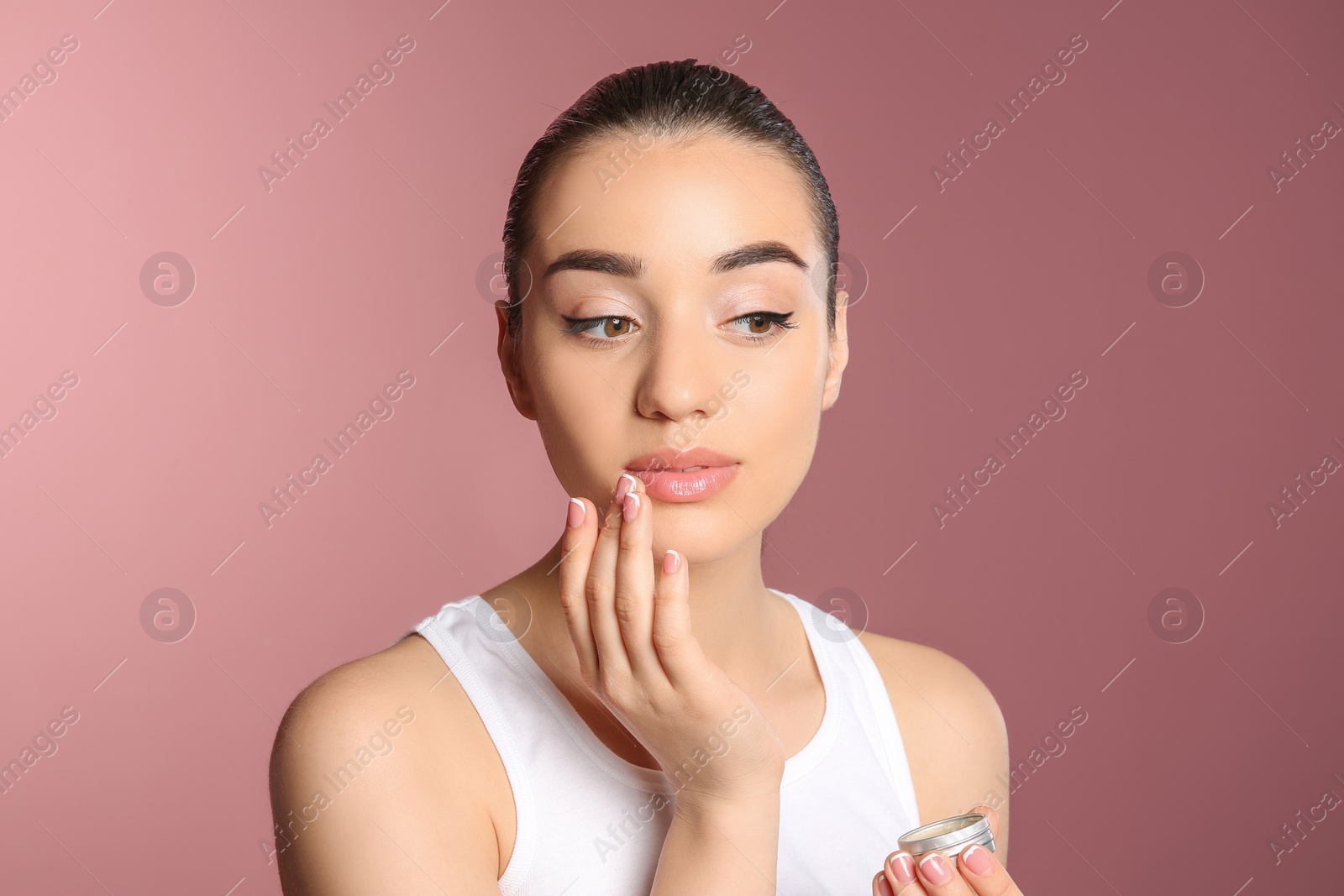 Photo of Young woman applying balm on her lips against color background