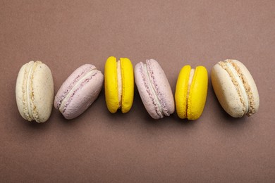 Delicious colorful macarons on brown background, flat lay