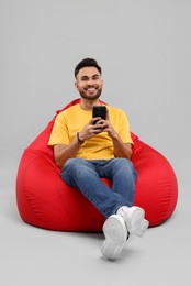 Happy young man using smartphone on bean bag chair against grey background