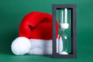 Photo of Hourglass and Santa hat on green background. Christmas countdown