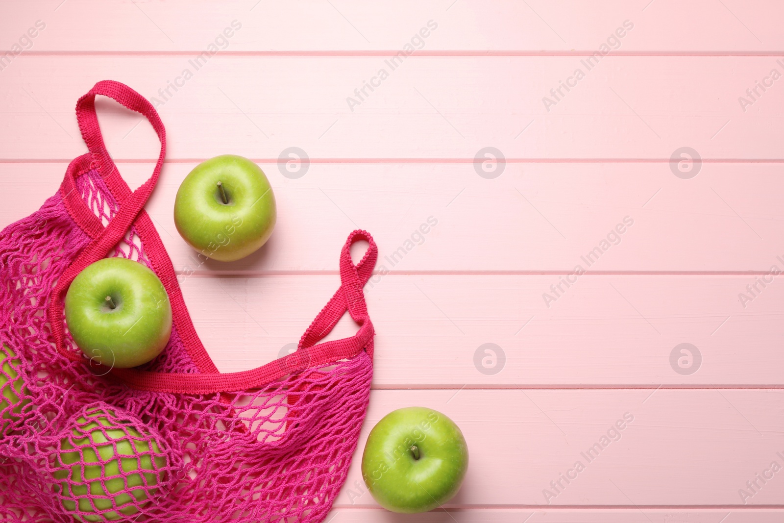 Photo of Net bag with fresh green apples on pink wooden table, flat lay. Space for text