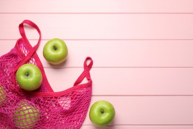 Net bag with fresh green apples on pink wooden table, flat lay. Space for text