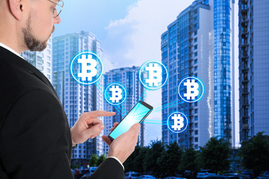 Fintech concept. Businessman using smartphone surrounded by bitcoin symbols on cityscape background