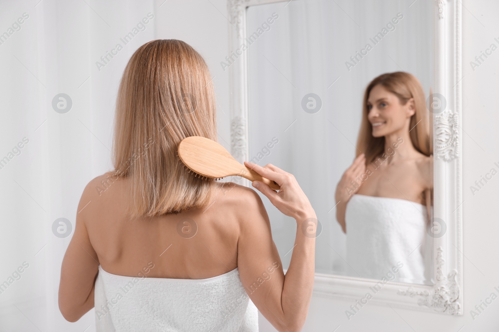 Photo of Woman after shower brushing her hair near mirror in room