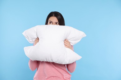 Young woman covering face with soft pillow on light blue background, space for text