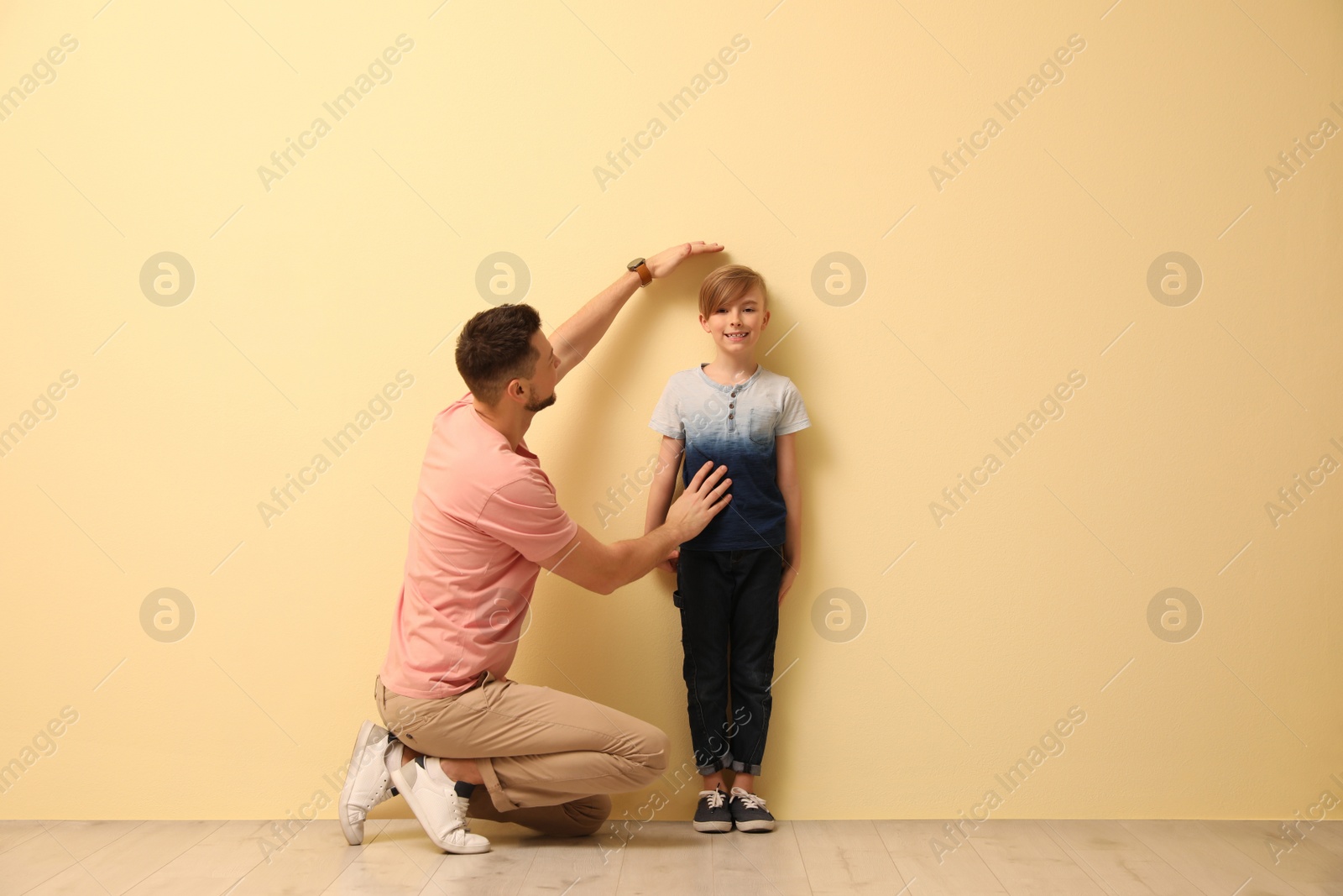 Photo of Father measuring height of his son near beige wall indoors