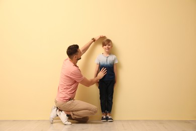 Photo of Father measuring height of his son near beige wall indoors
