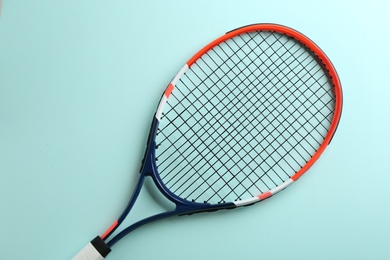 Tennis racket on light blue background, top view. Sports equipment