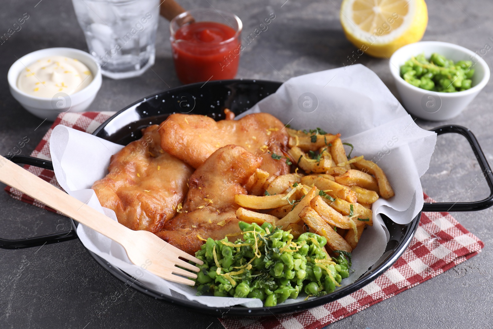 Photo of Tasty fish, chips, sauces and peas on grey table, closeup