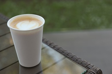 Photo of Cardboard takeaway cup of coffee on glass table outdoors, space for text