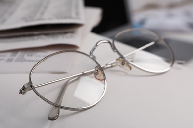 Photo of Glasses and newspapers on armrest indoors, closeup