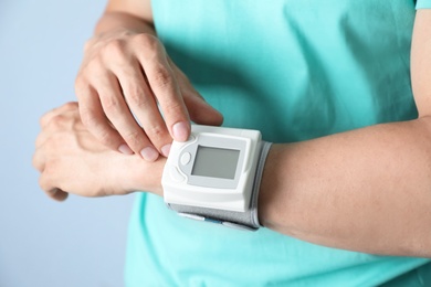 Young man checking pulse with blood pressure monitor on wrist against color background, closeup