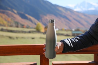 Photo of Boy holding thermo bottle with drink in mountains on sunny day, closeup