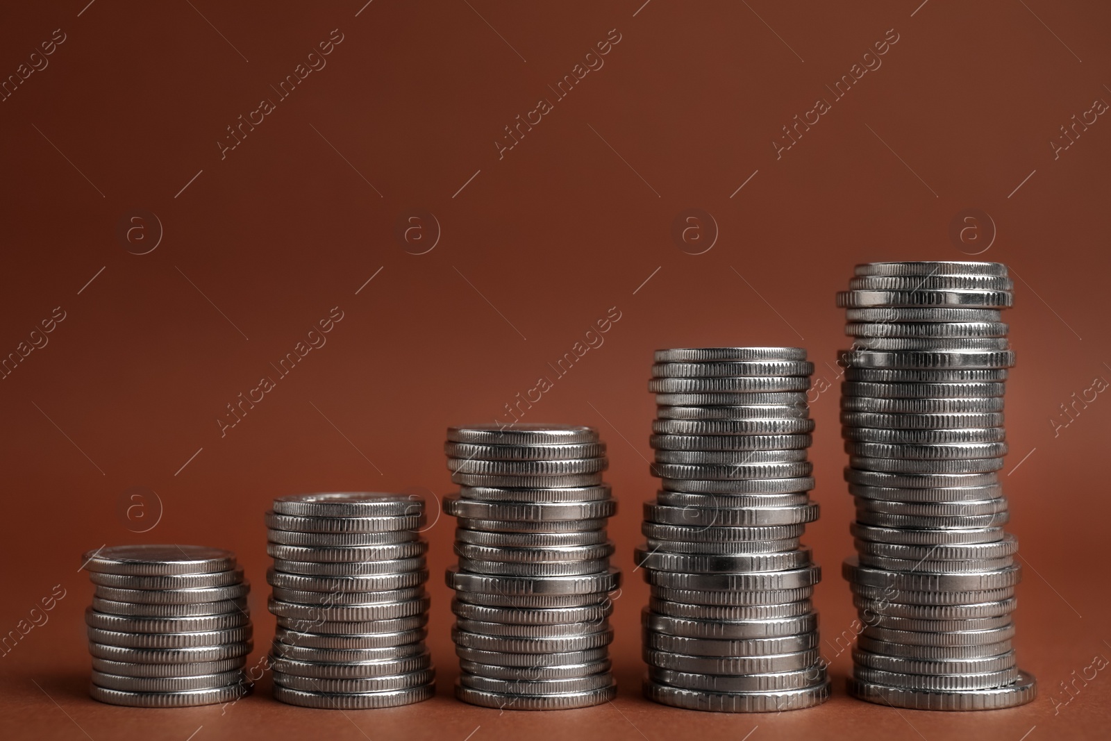 Photo of Many silver coins stacked on brown background, space for text
