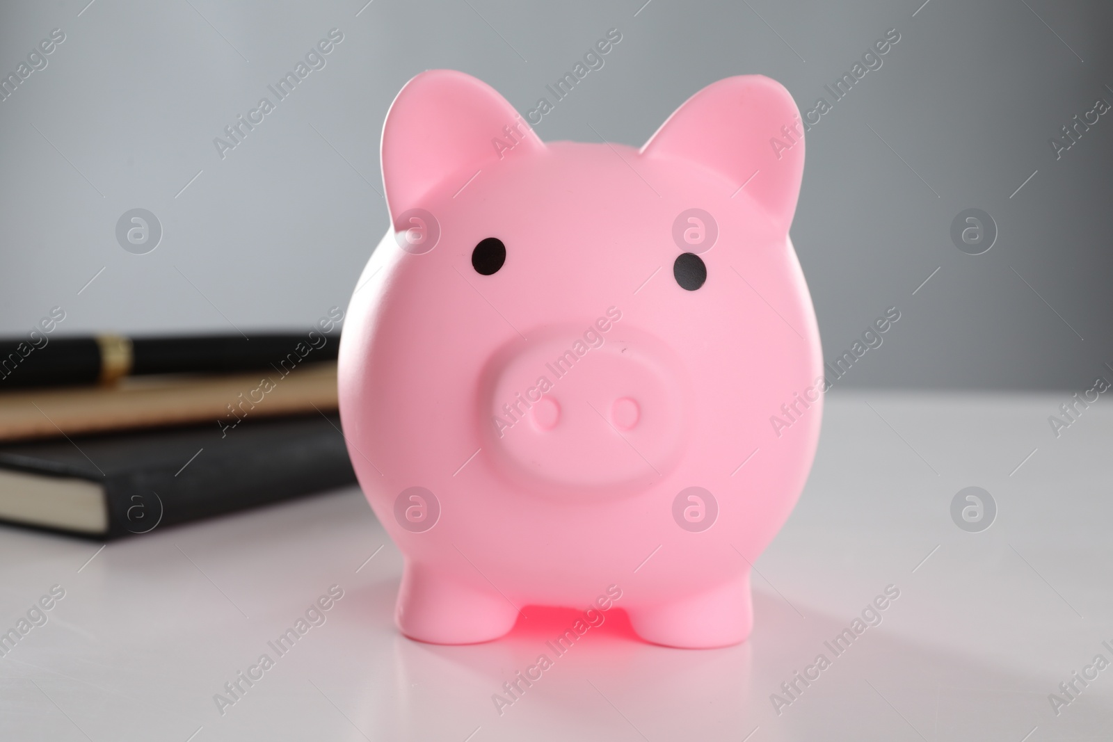 Photo of Pink piggy bank and books on white table