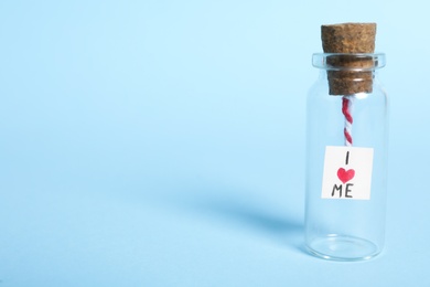 Photo of Piece of paper with phrase I Love Me in small glass bottle on light blue background, space for text