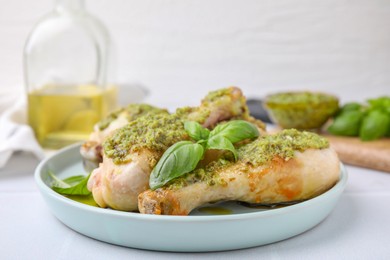 Delicious fried chicken drumsticks with pesto sauce and basil on white table, closeup
