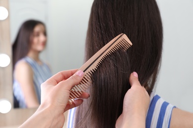 Photo of Woman combing friend's hair indoors, closeup view