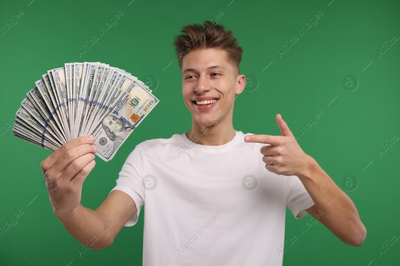 Photo of Happy man pointing at dollar banknotes on green background