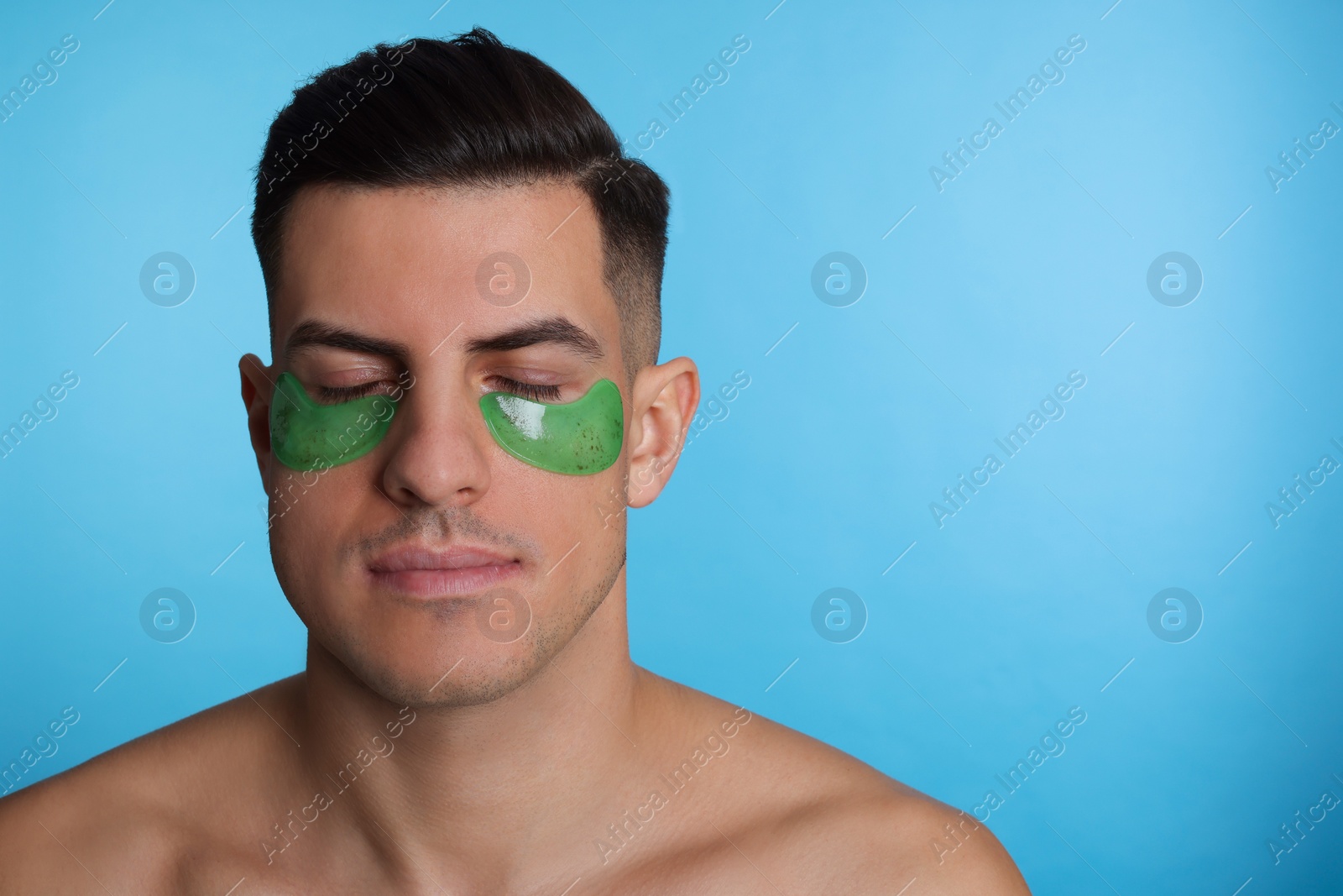 Photo of Man with green under eye patches on light blue background. Space for text