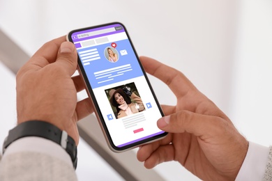 Young man visiting online dating site via smartphone indoors, closeup