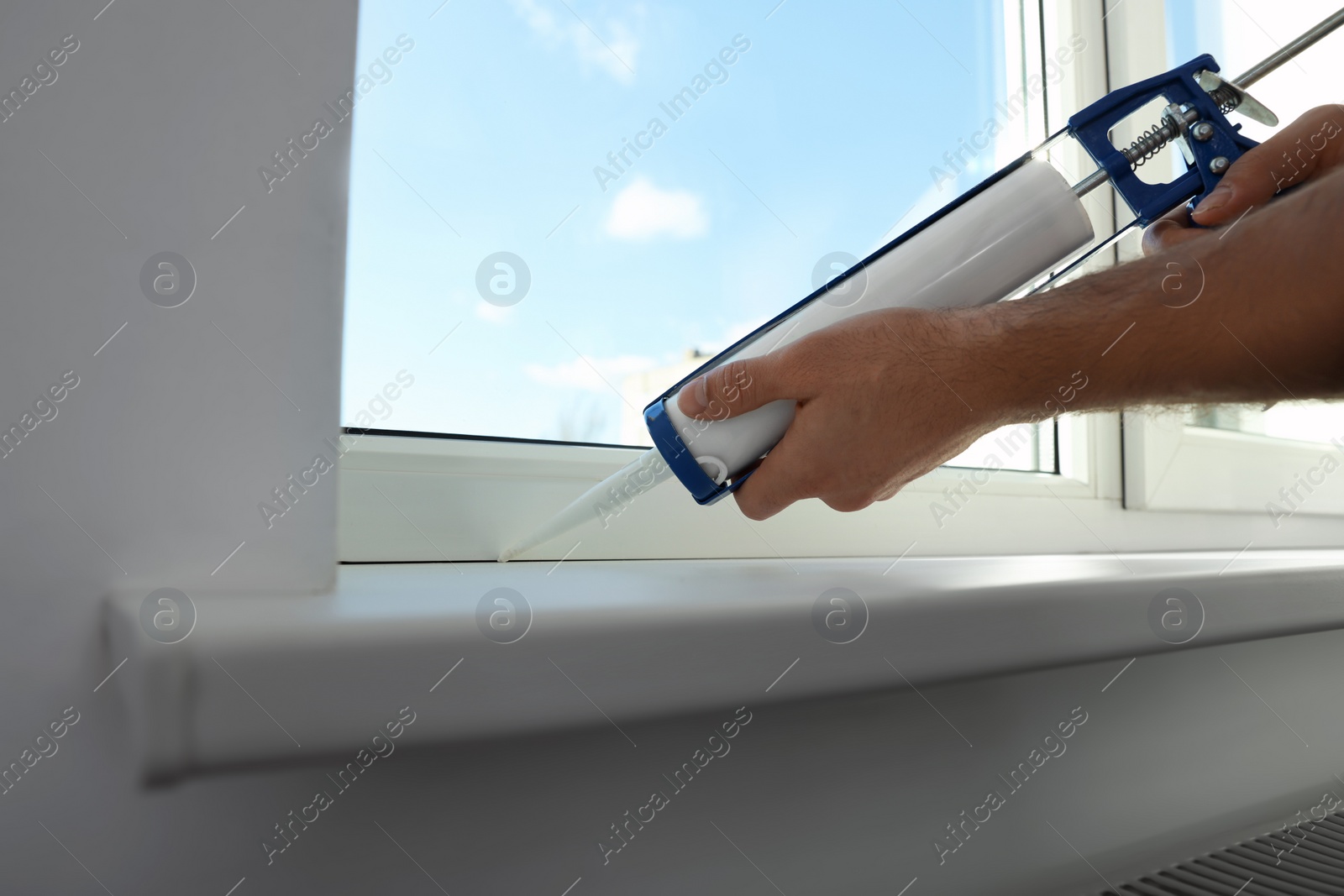 Photo of Man sealing window with caulk indoors, closeup