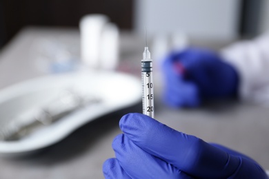 Photo of Doctor holding syringe against blurred background, closeup with space for text. Medical objects