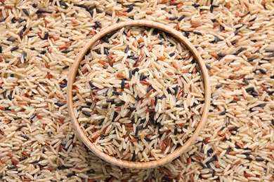 Photo of Mix of different brown rice and wooden bowl, top view