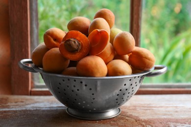 Photo of Colander with delicious ripe apricots on wooden table near window