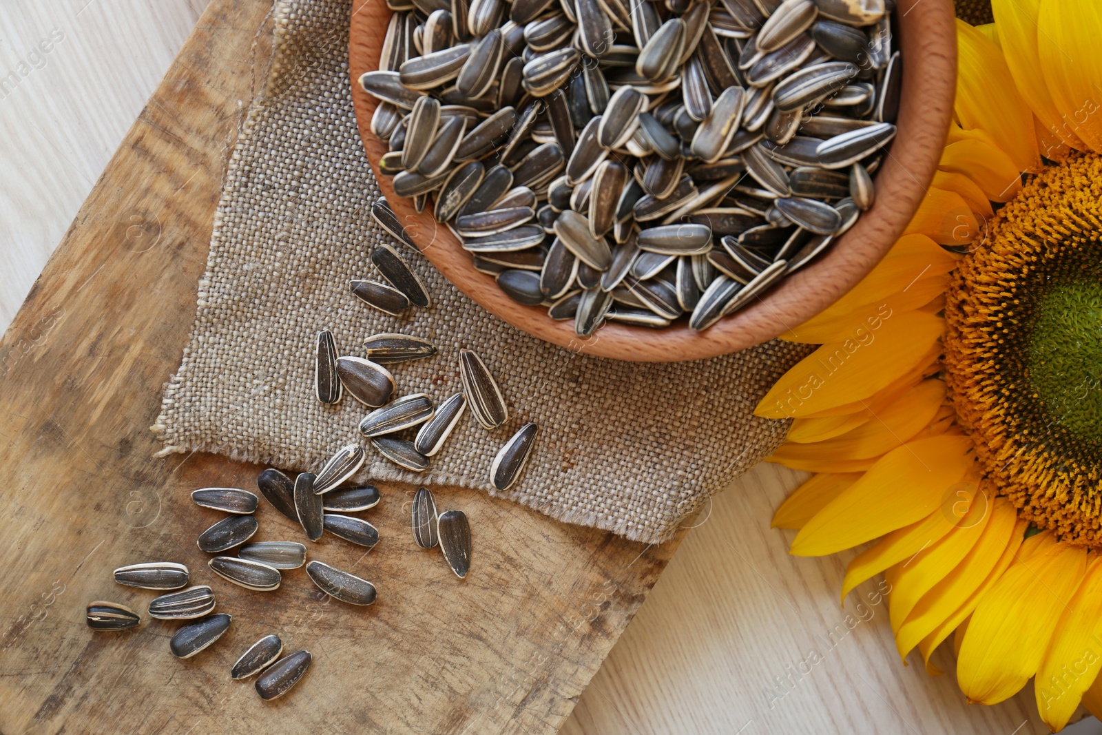 Photo of Organic sunflower seeds and flower on wooden table, flat lay